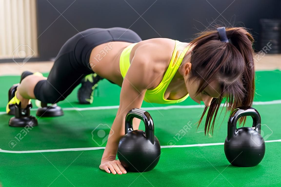 Fit woman young doing push ups exercise with dumbbells in the gym.