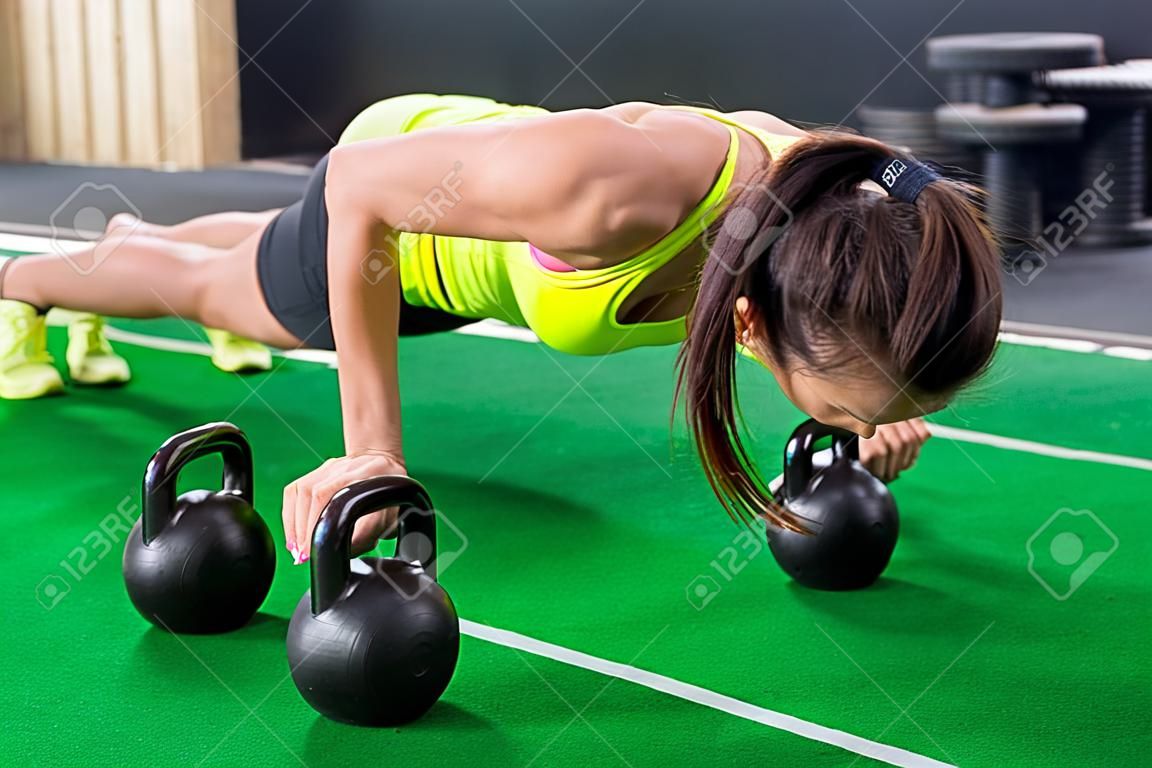 Fit woman young doing push ups exercise with dumbbells in the gym.