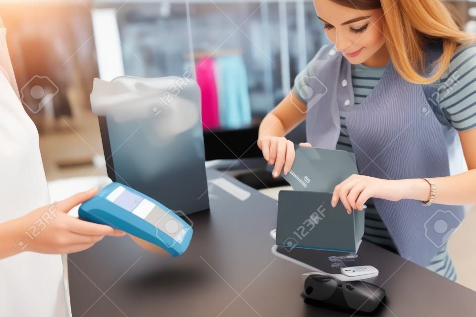 Cliente femenino joven que se coloca en el escritorio de efectivo que paga con la tarjeta de crédito en tienda de la ropa