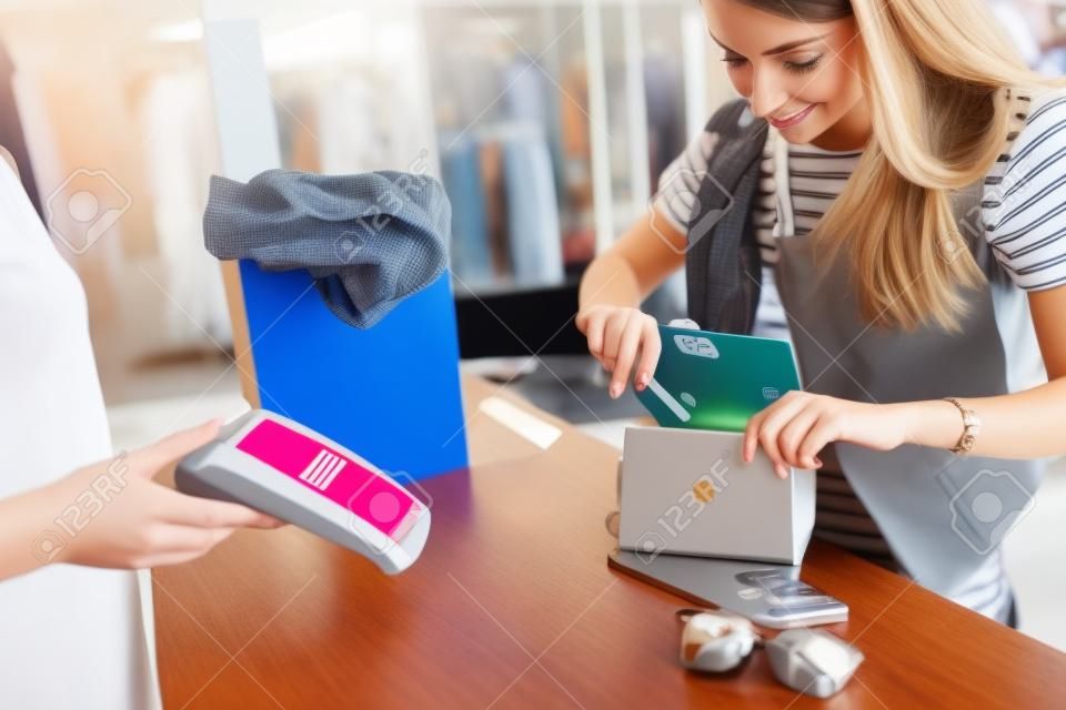 Cliente femenino joven que se coloca en el escritorio de efectivo que paga con la tarjeta de crédito en tienda de la ropa