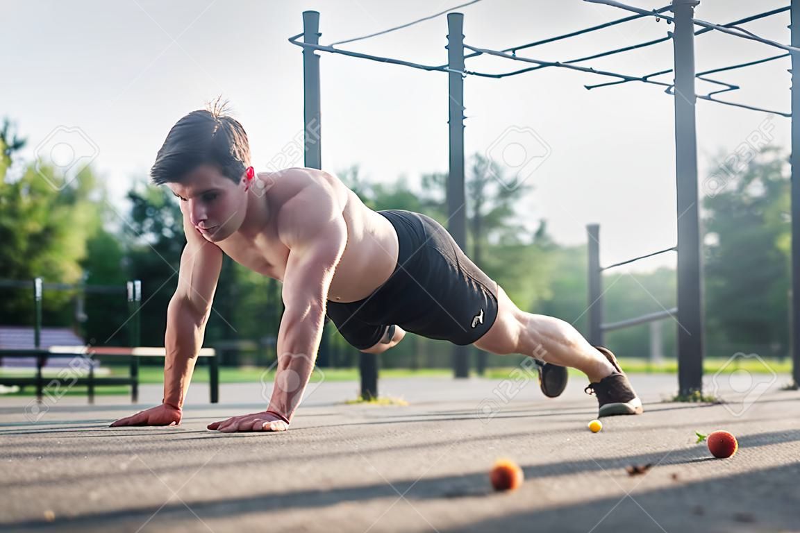 Athlète jeune homme faisant un exercice de bras-push à un bras travaillant ses muscles du haut du corps à l'extérieur en été.