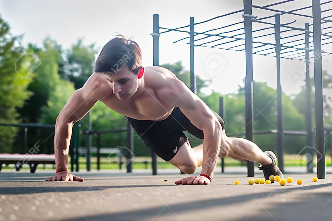 Athlète jeune homme faisant un exercice de bras-push à un bras travaillant ses muscles du haut du corps à l'extérieur en été.