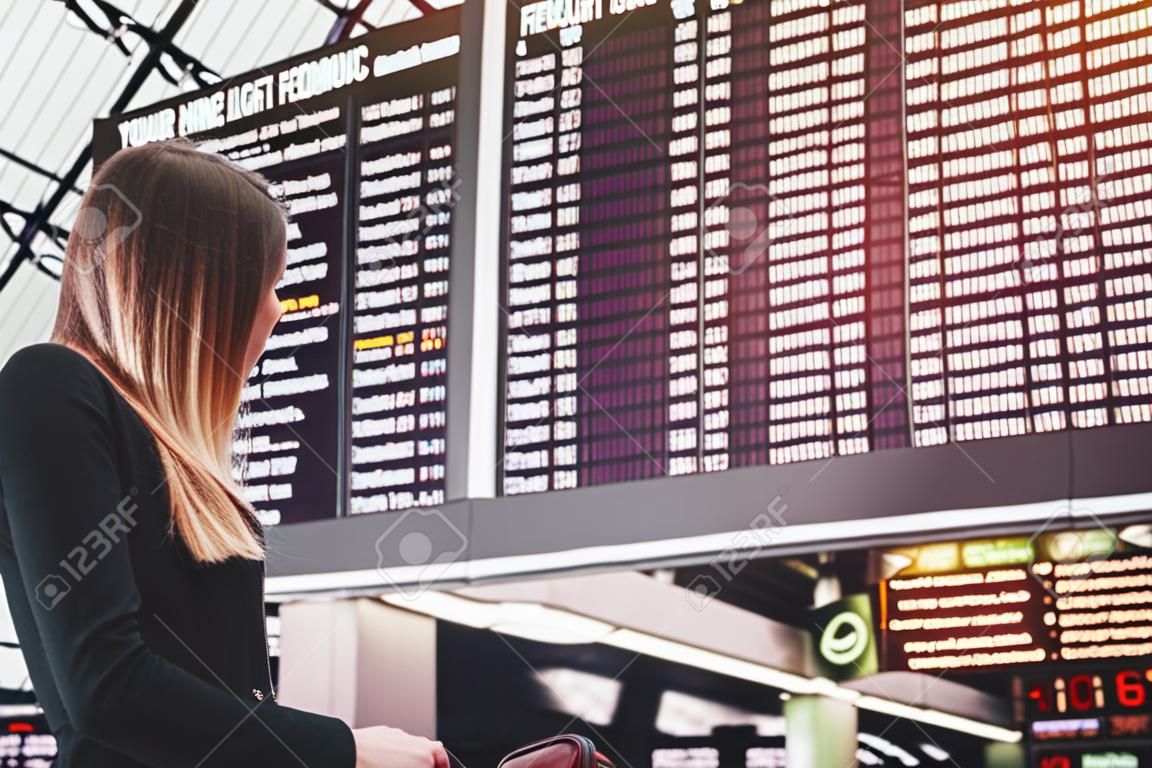 Young woman standing against flight scoreboard in airport