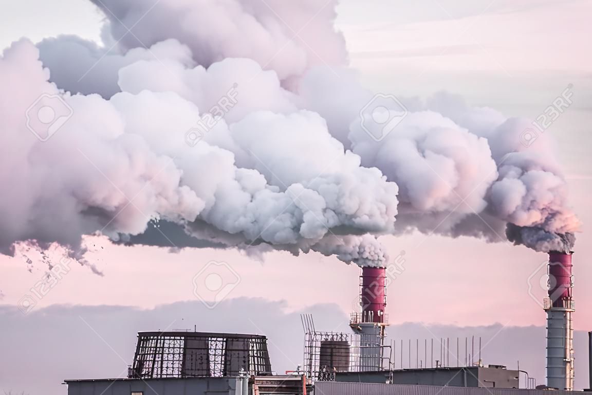 chaminés industriais com fumaça pesada que causa a poluição do ar como um problema ecológico no fundo do céu cor-de-rosa do pôr-do-sol