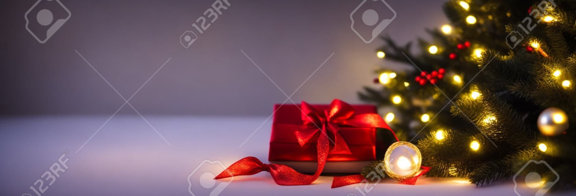 Christmas coziness in a room on a light background, with lights and branches of a Christmas tree and a gift with a red bow on the table, space for text