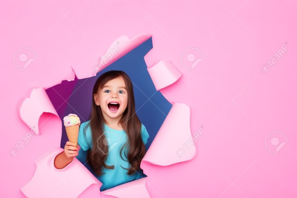 funny little girl peeking out of the hole with ice cream in her hands, on a colored pink background, space for text, Studio shooting