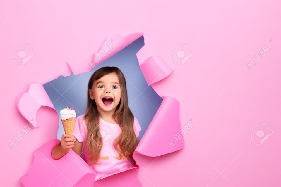divertente bambina che sbircia fuori dal buco con il gelato in mano, su uno sfondo rosa colorato, spazio per il testo, riprese in studio