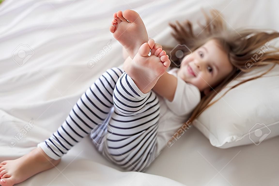 Cute little fun girl with long hair in bed woke up in the morning . Concept of sleep and development of children.