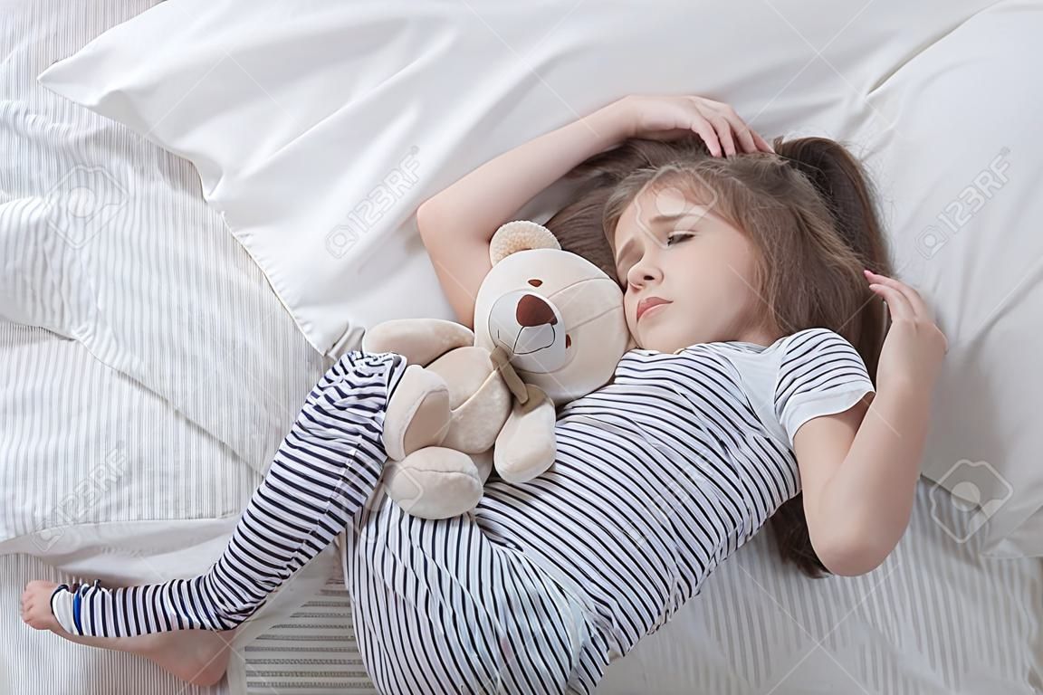 Nettes kleines Mädchen im weißen Bett, trauriges umarmendes weiches Bärenspielzeug. Konzept des Schlafes und der Entwicklung von Kindern.