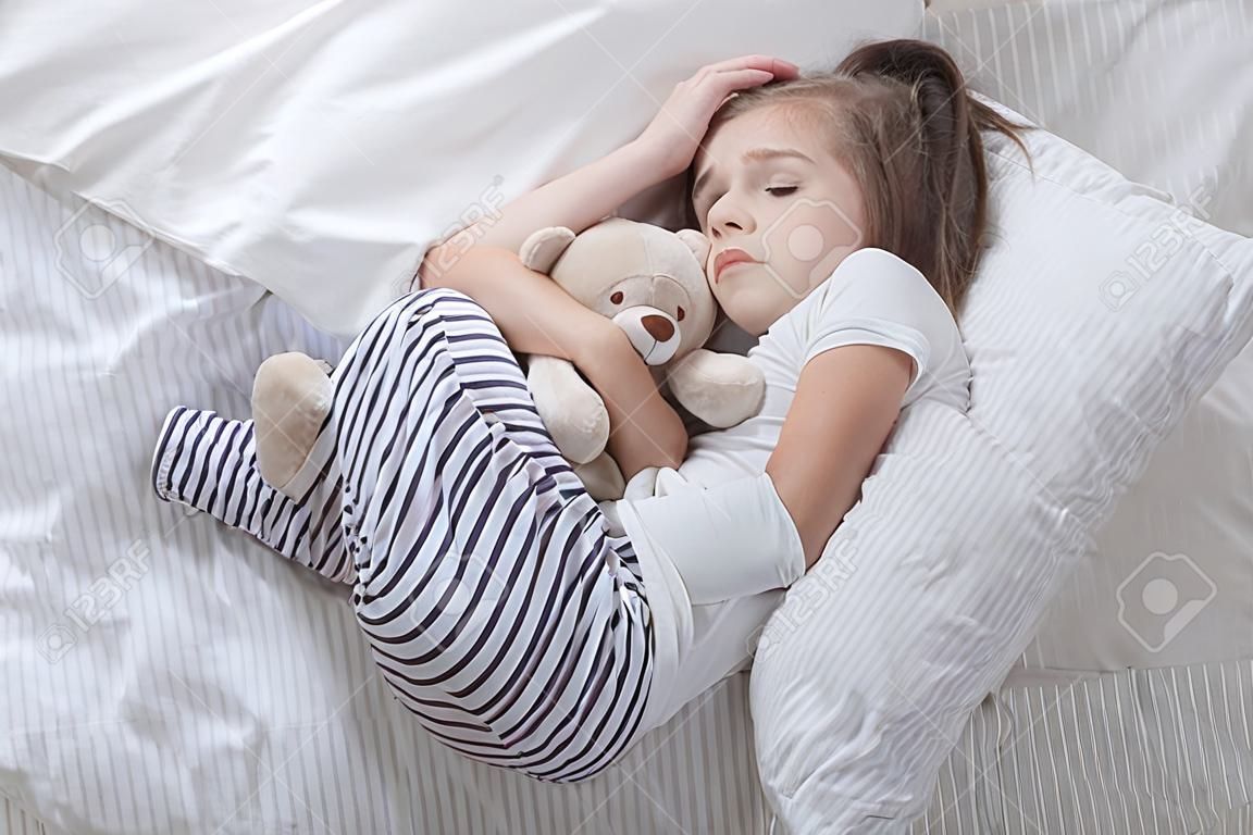 Nettes kleines Mädchen im weißen Bett, trauriges umarmendes weiches Bärenspielzeug. Konzept des Schlafes und der Entwicklung von Kindern.