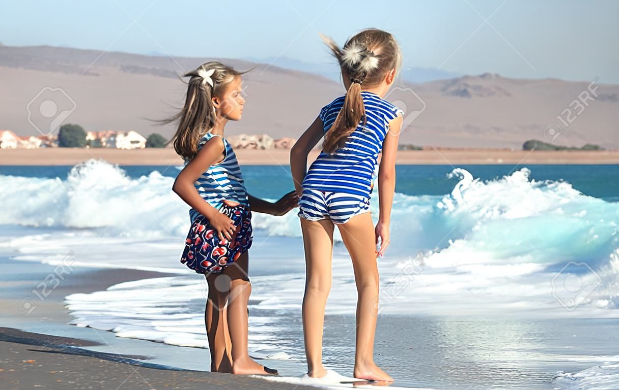 Two little girls play along the beach by the sea. The concept of friendship and recreation.