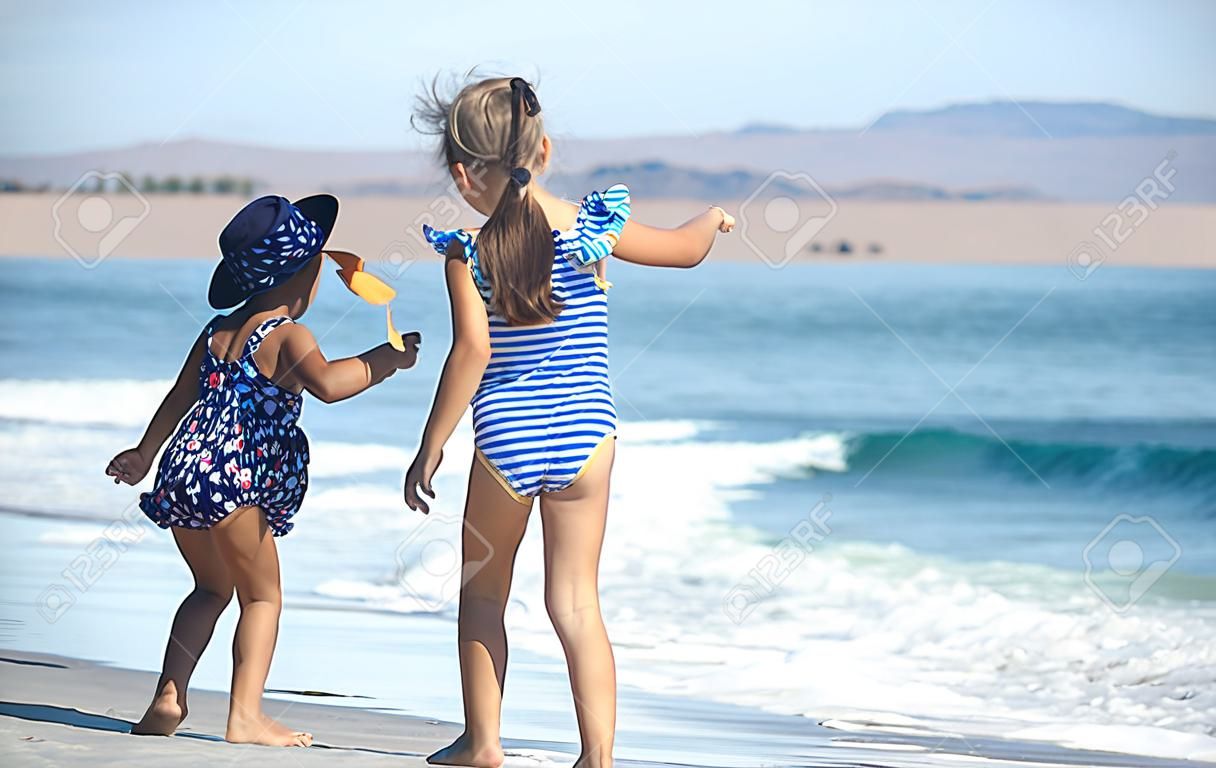 Two little girls play along the beach by the sea. The concept of friendship and recreation.
