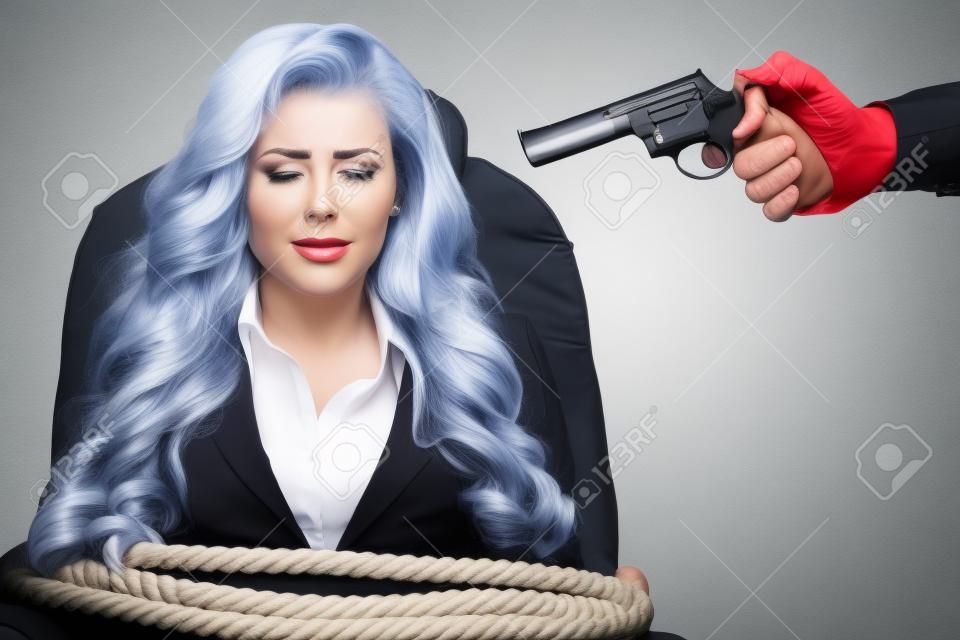 Mujer de negocios atada a una silla con una cuerda y apuntar a la cabeza con una pistola aislado sobre un fondo blanco