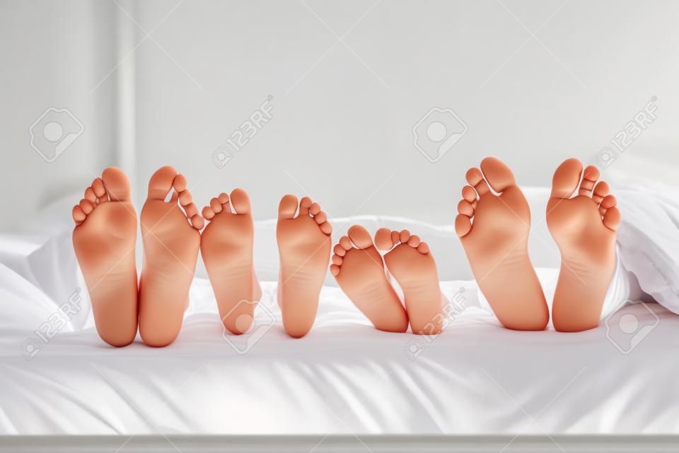母親，父親和兩個孩子躺在床上，白色的床單;專注於腳