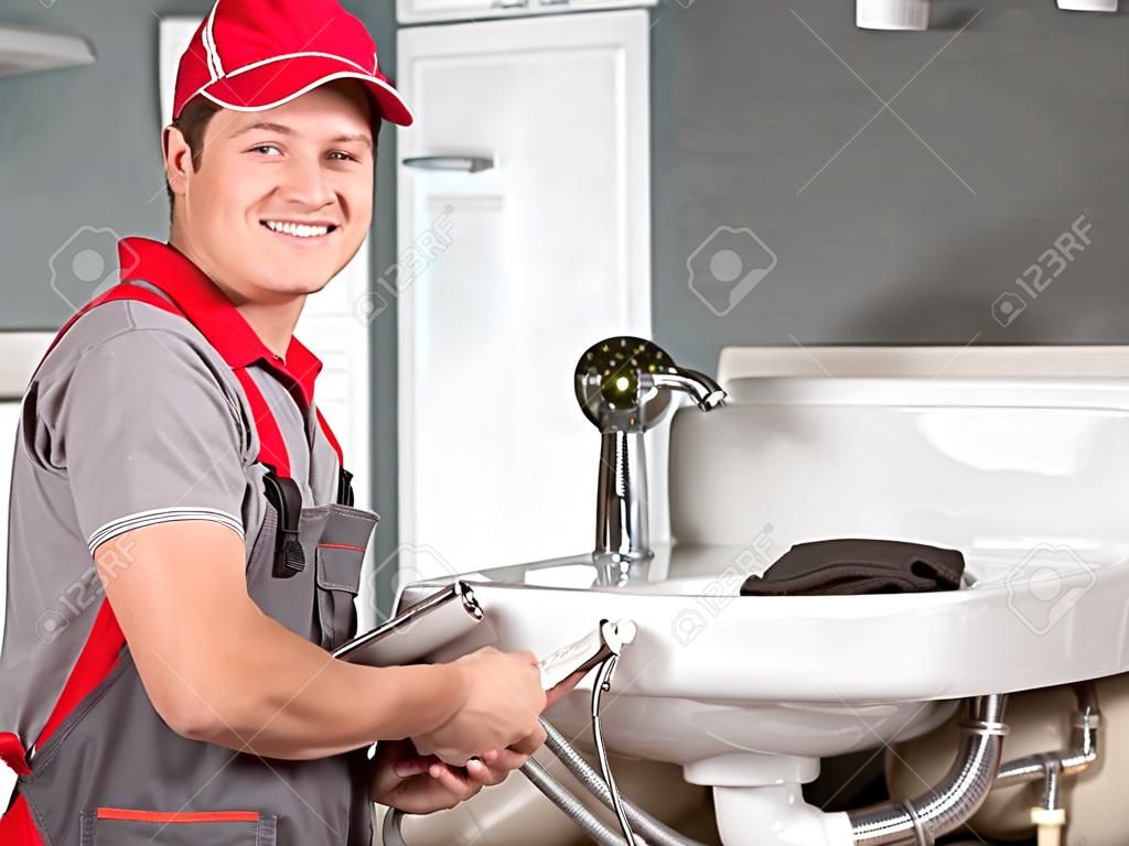 Plumber standing in front of washbasin writing on clipboard.