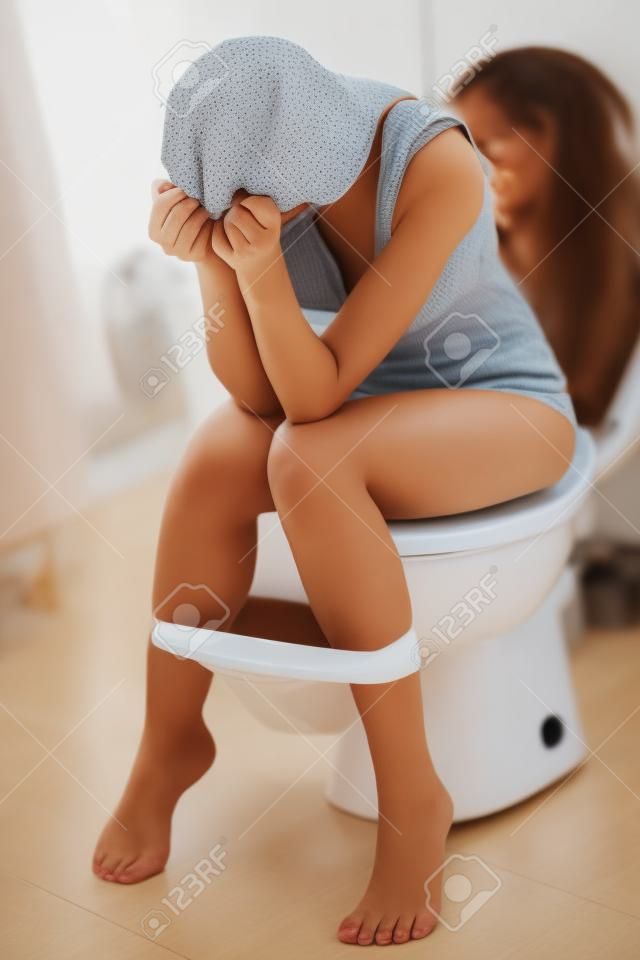 женщина, сидящая на туалете в ванной комнате. используя смартфон. домашний халат