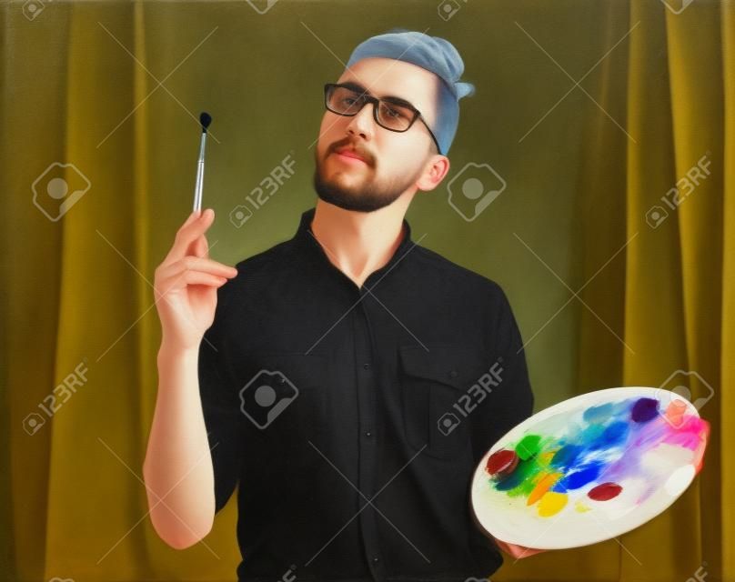 Retrato de un artista masculino joven está sosteniendo un pincel y mezclar la pintura al óleo de color en la paleta.