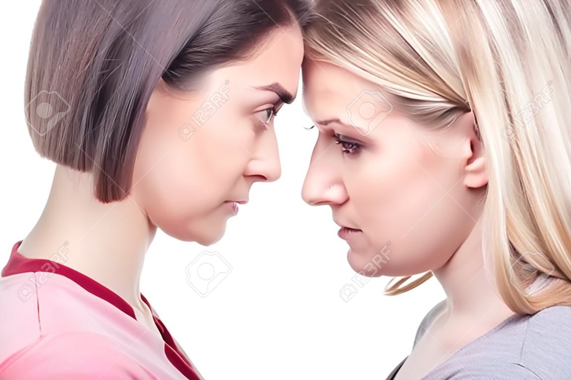Close-up portrait young angry women are standing forehead to forehead. Oppose each other. Isolated white background.
