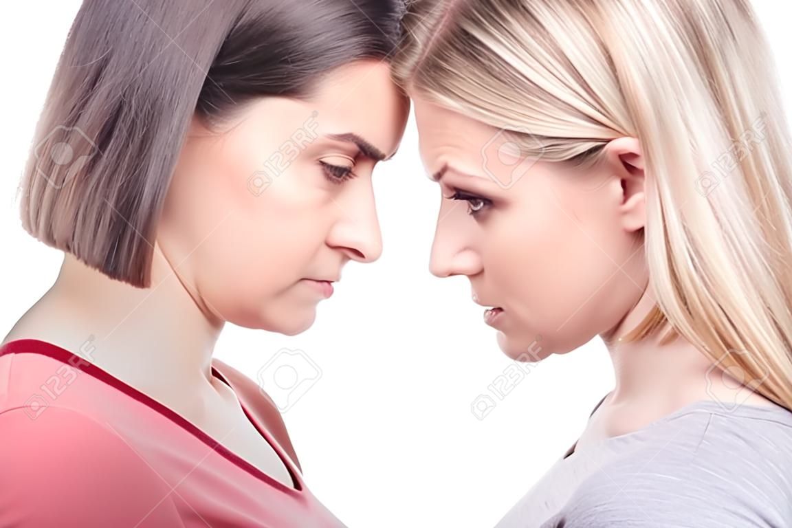 Close-up portrait young angry women are standing forehead to forehead. Oppose each other. Isolated white background.