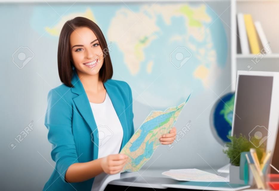 若い女性の肖像画は旅行代理店のオフィスに座っている地図を使用して移動する場所を選択します。