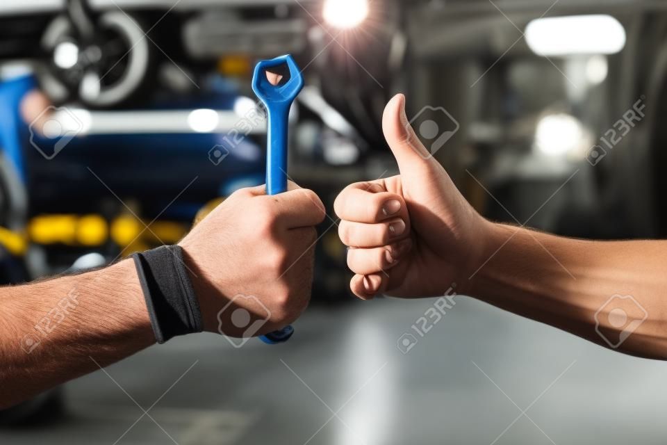 Immagine ritagliata di meccanici che lavorano nel servizio di auto. Uno tiene in mano una chiave mentre l'altro mostra il segno Ok