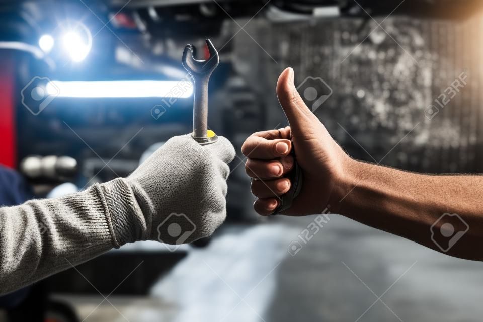 Immagine ritagliata di meccanici che lavorano nel servizio di auto. Uno tiene in mano una chiave mentre l'altro mostra il segno Ok