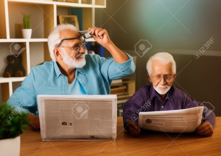 Дедушка и внук отдыхают дома. Красивый старик использует ноутбук, пока его мальчик читает газету