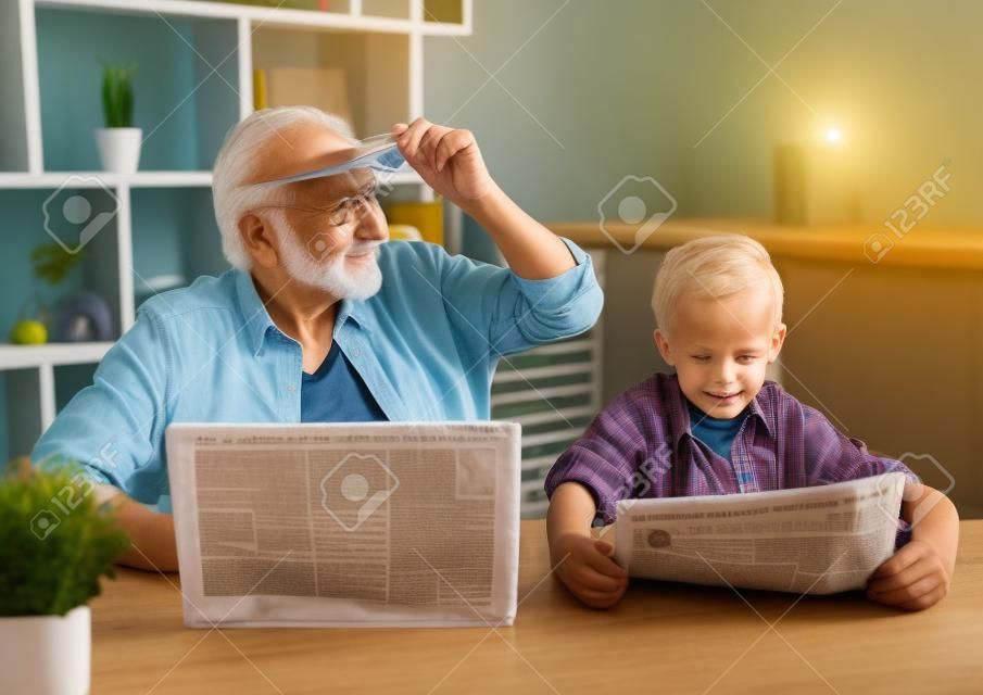 Opa en kleinzoon rusten thuis. Knappe oude man gebruikt een laptop terwijl zijn jongen een krant leest