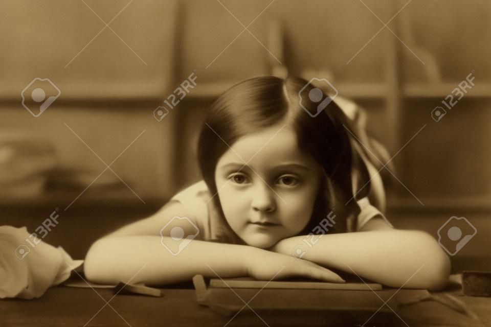 The girl is lying on the table, her head resting on crossed arms and looking indifferently ahead