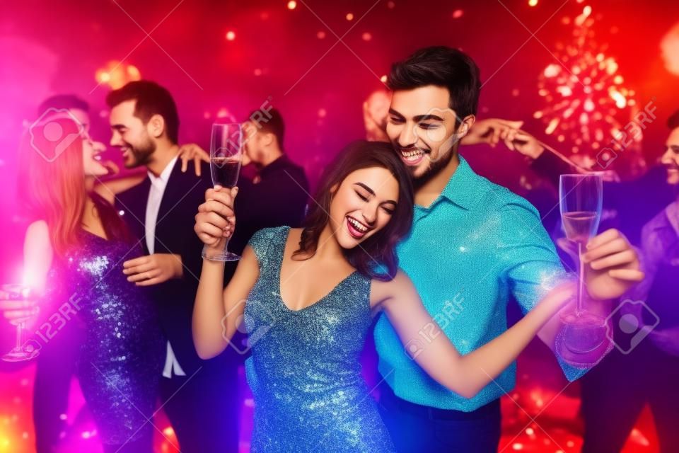 Os jovens se divertem em uma festa de Ano Novo. Em primeiro plano, um casal está dançando com óculos nas mãos.