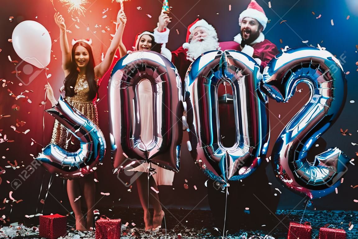 Smiling People with Baloons Celebrating New Year. Celebrating of New Year. Young Woman in Dress. Young Man in Santa Claus Suit. People with Gray Baloons. Happy New Year. People Have Fun.