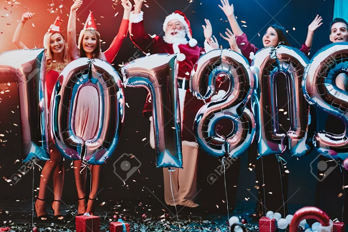Smiling People with Baloons Celebrating New Year. Celebrating of New Year. Young Woman in Dress. Young Man in Santa Claus Suit. People with Gray Baloons. Happy New Year. People Have Fun.