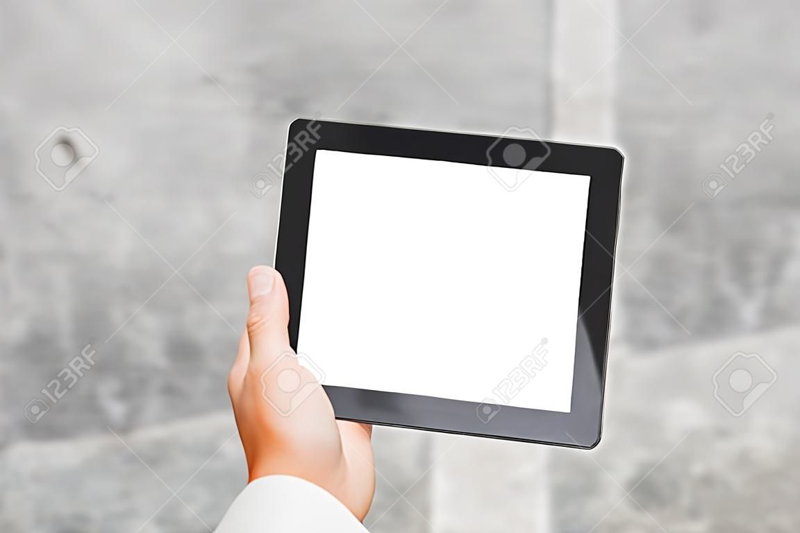 Nahaufnahme eines Tablet-Modells mit einem weißen Bildschirm in den Händen eines Geschäftsmanns vor dem Hintergrund einer Betonwand