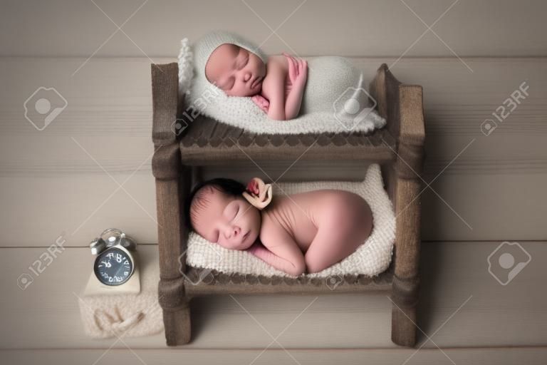 밝은 나무 배경에 흰색 바디슈트를 입은 작은 신생아 쌍둥이 소년. 신생아 쌍둥이는 이층 나무 침대에서 잔다. 소년들은 흰 모자를 쓰고 있습니다. 출생 시간이 표시된 시계. 스튜디오 사진.