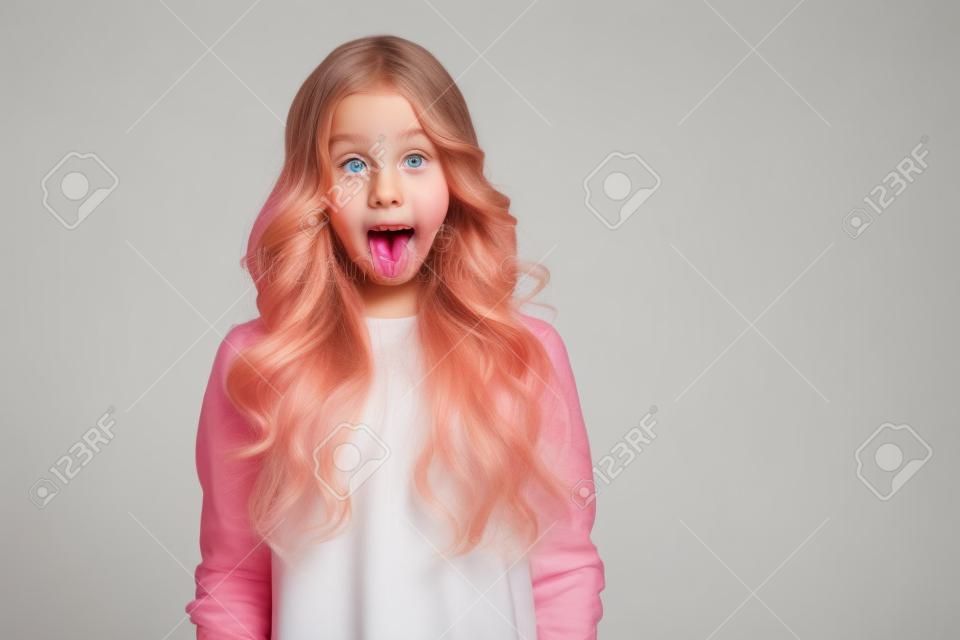 Retrato de uma menina bonita jovem que mostra a língua isolada em um fundo branco