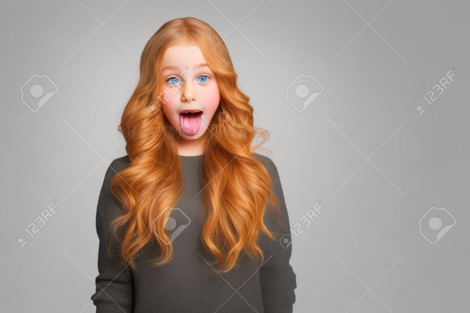Retrato de uma menina bonita jovem que mostra a língua isolada em um fundo branco
