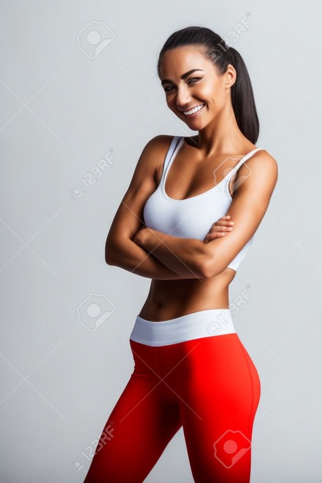 Portrait of a smiling fitness woman standing with arms folded and looking at camera isolated on a white background