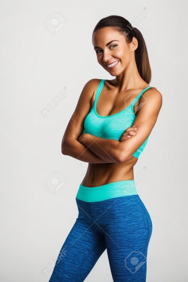 Portrait of a smiling fitness woman standing with arms folded and looking at camera isolated on a white background