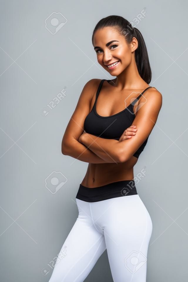 Portrait d'une femme de remise en forme en souriant debout avec les bras croisés et regardant la caméra isolée sur un fond blanc