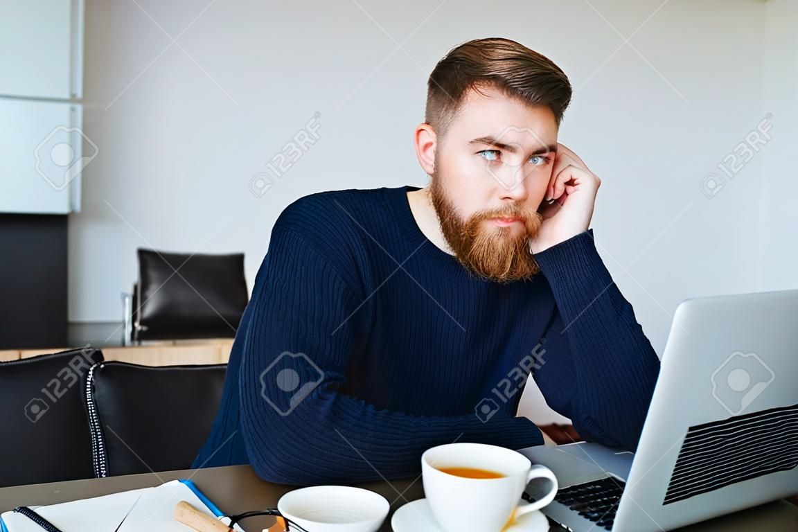 Portrait of a pensive man sitting at the table with laptop computer at home