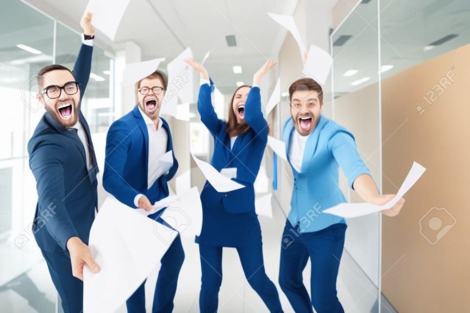 Group of joyful excited business people throwing papers and having fun in office