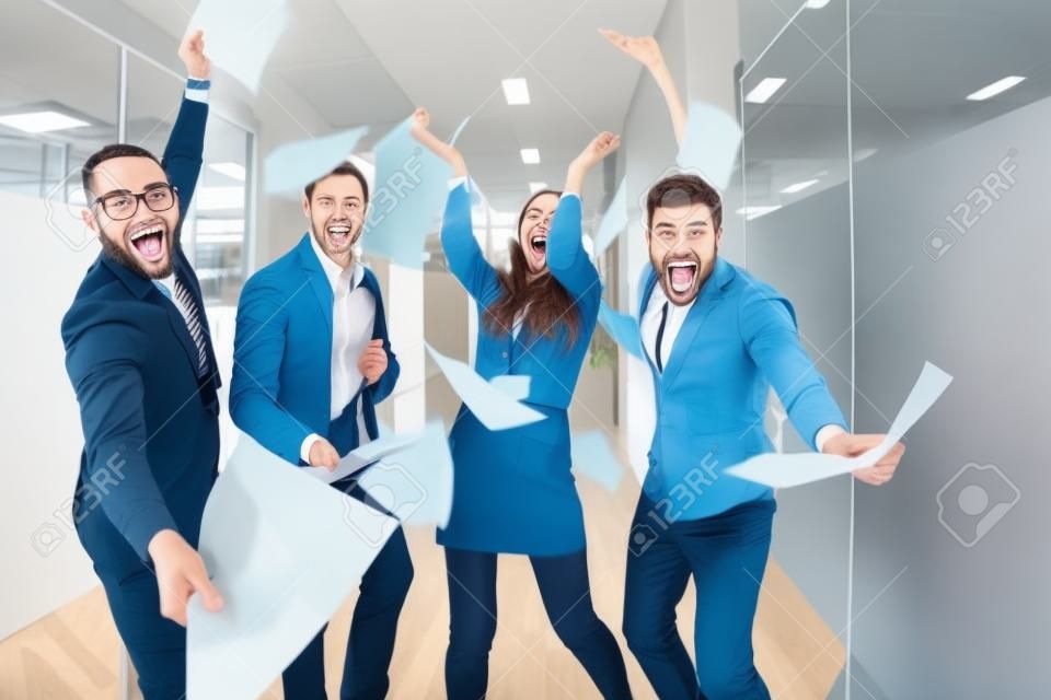 Grupa ludzi biznesu wzbudzonych radosne rzucanie papiery i zabawy w biurze