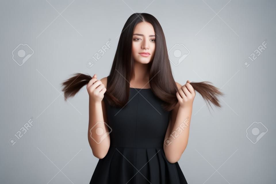 Upset bella giovane donna in piedi e guardando le spaccature estremità dei suoi lunghi capelli scuri su sfondo bianco