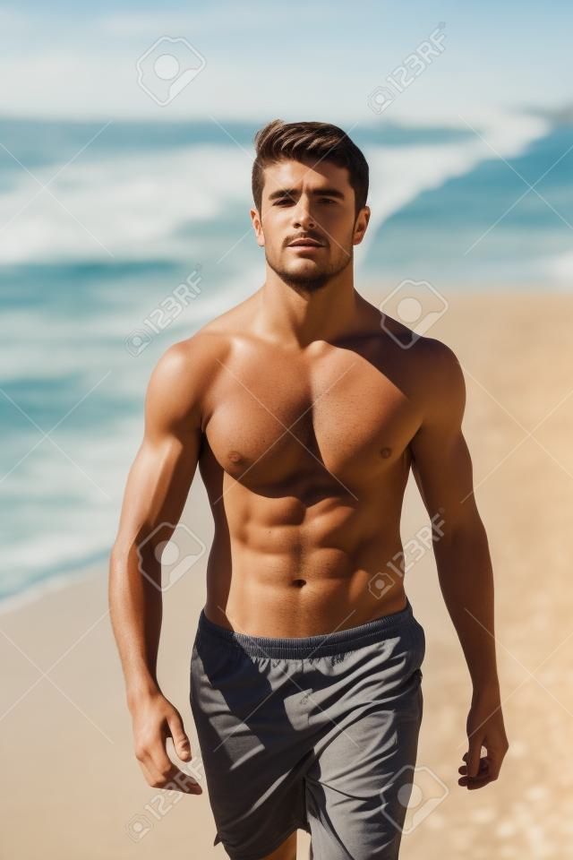 Primo piano di fiducioso giovane uomo a torso nudo che cammina lungo la spiaggia