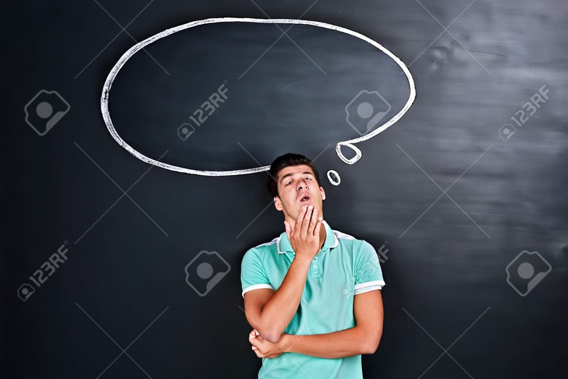 Bored tired young man standing and yawning over chalkboard background