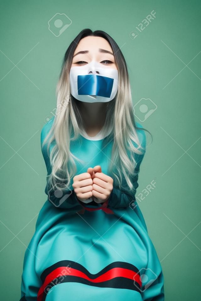 Mujer delimitado por cuerdas que se sienta con la boca cerrada por la cinta y que pide ayuda