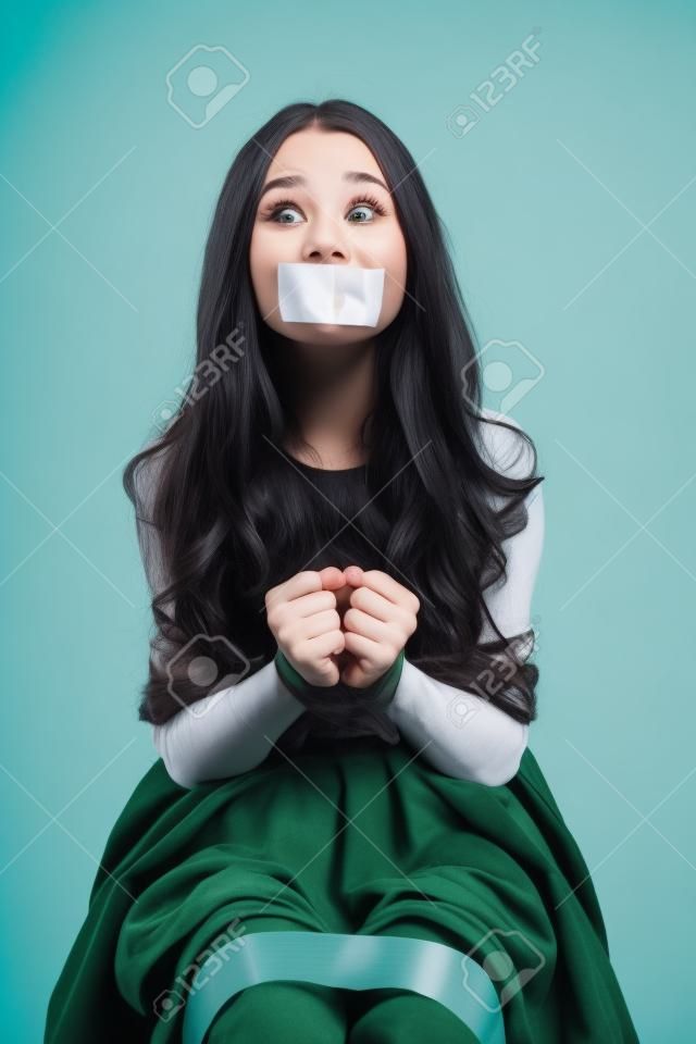 Giovane donna spaventata legata da corde sedute con la bocca chiusa da nastro