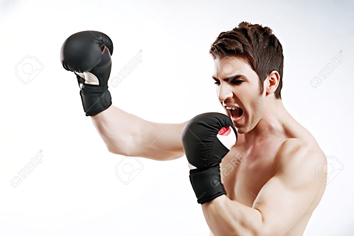 Photo of screaming young man boxer make boxing exercises over white background. Look aside.