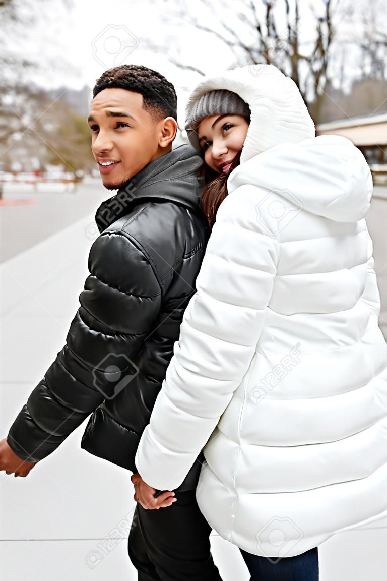 Cheerful young couple holding hands and looking back outdoors in winter