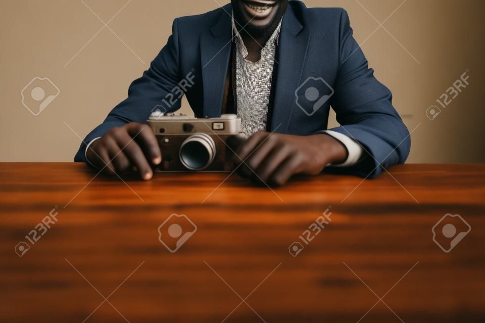 imagen recortada del hombre africano en traje sentado junto a la mesa con cámara retro